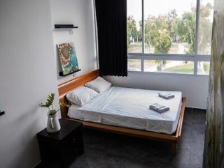 A cozy bedroom with a large bed, simple furnishings, and a window view of greenery.